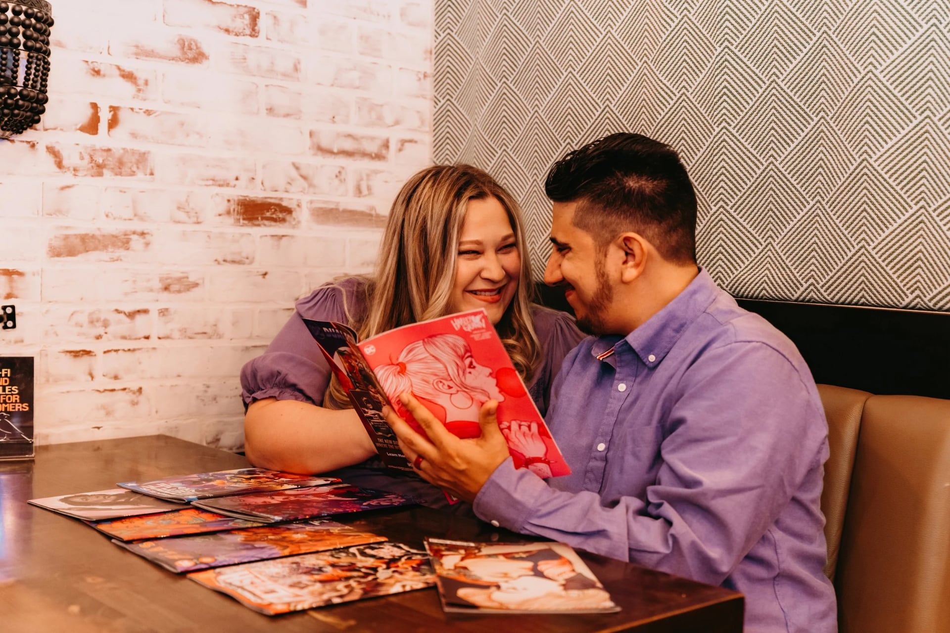 owners Lauren and Danny sitting at a table and smiling together while reading a comic book